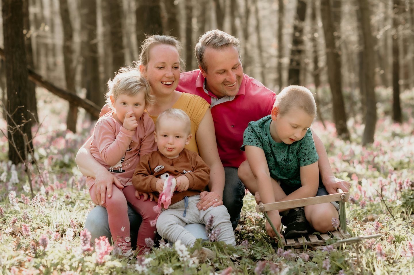 Famiglia europea sorridente in una foresta soleggiata con fiori.